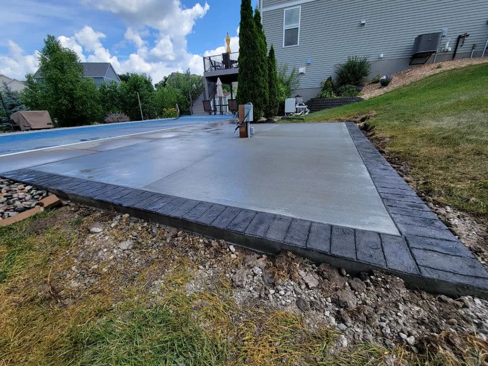 Concrete patio with dark stone border and landscaped yard, ideal for outdoor living space.