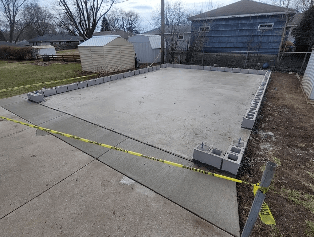 Concrete foundation with cinder blocks, marked by caution tape, in a residential yard.