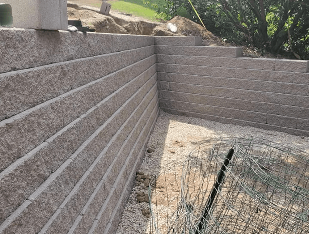 Retaining wall construction with textured blocks and gravel base in a landscaped area.