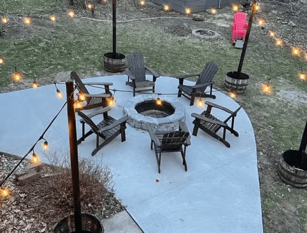 Cozy outdoor fire pit setup with Adirondack chairs and string lights in a backyard.