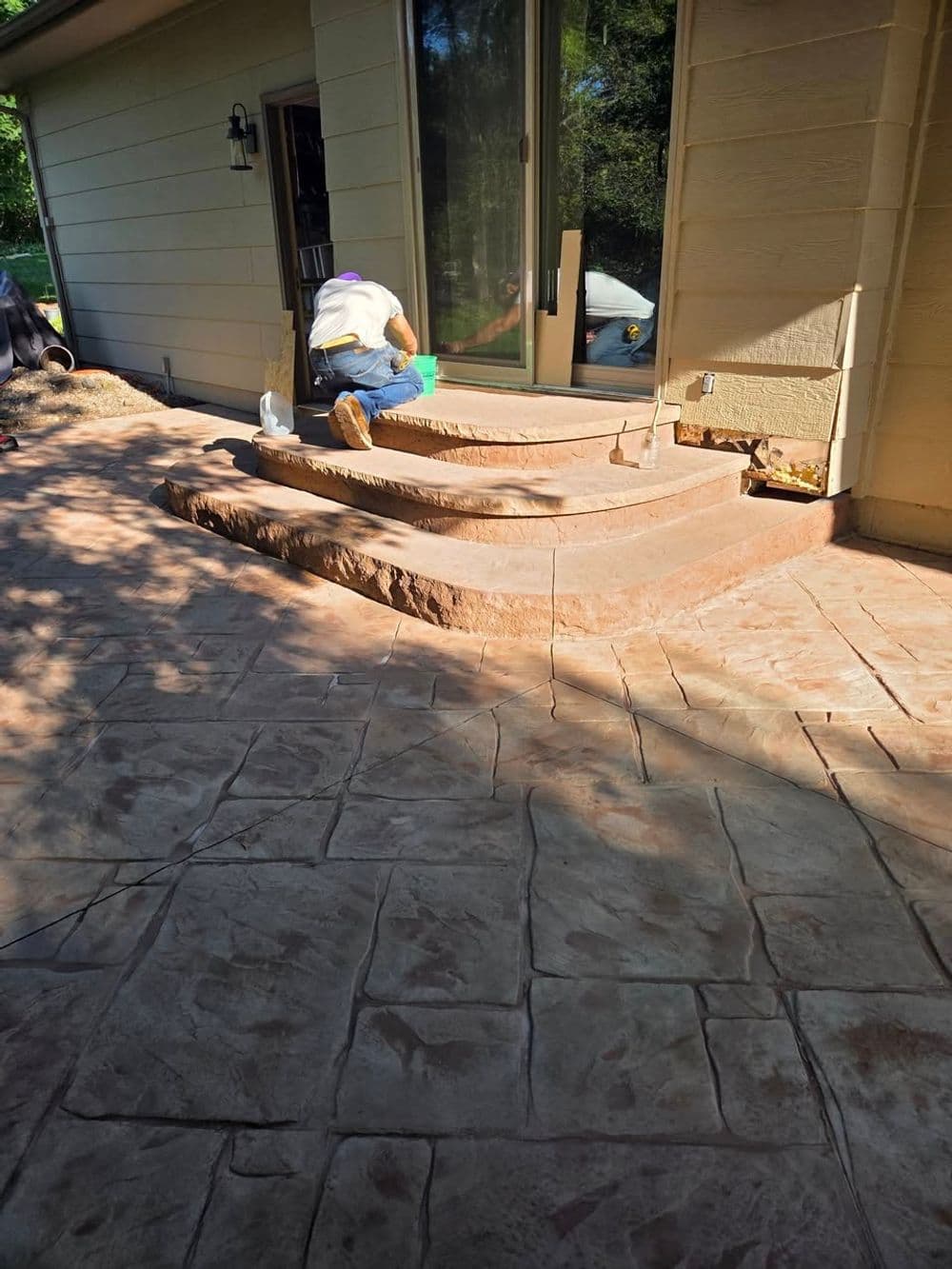 Worker applying finishing touches on decorative concrete steps and patio outside a home.