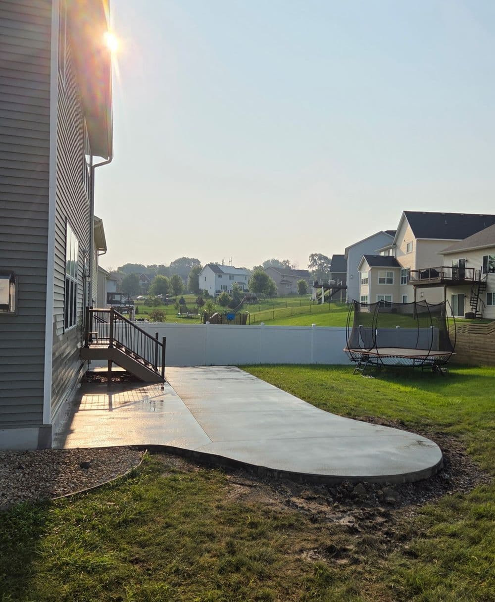 Backyard view featuring a newly poured concrete patio and trampoline near a suburban home.