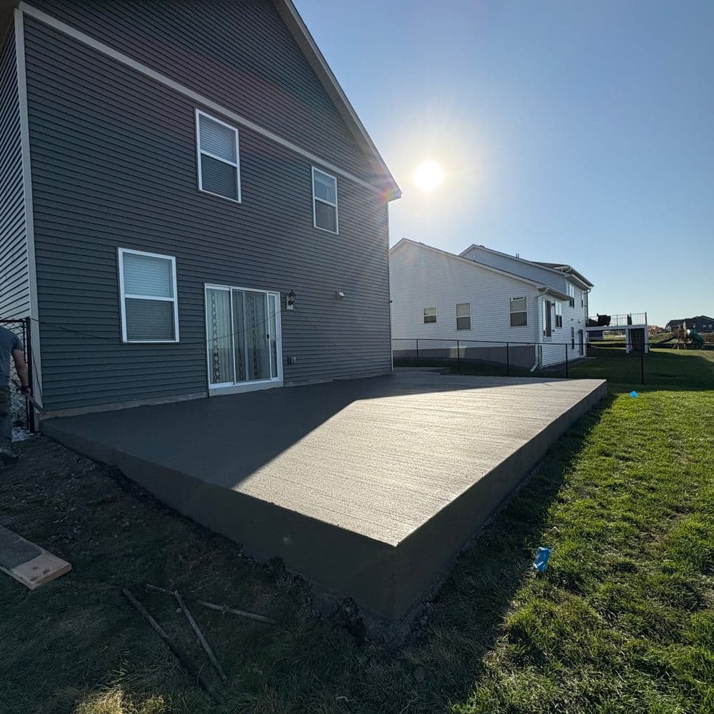 Newly poured concrete patio in a residential backyard with adjacent houses and clear blue sky.