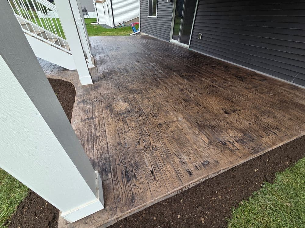 Stamped concrete patio with a wood-like finish, surrounded by grass and a modern home exterior.