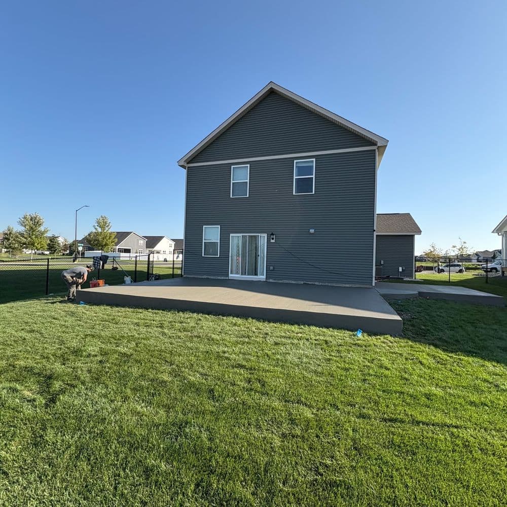 Modern gray house with a patio, green lawn, and clear blue sky in a suburban neighborhood.