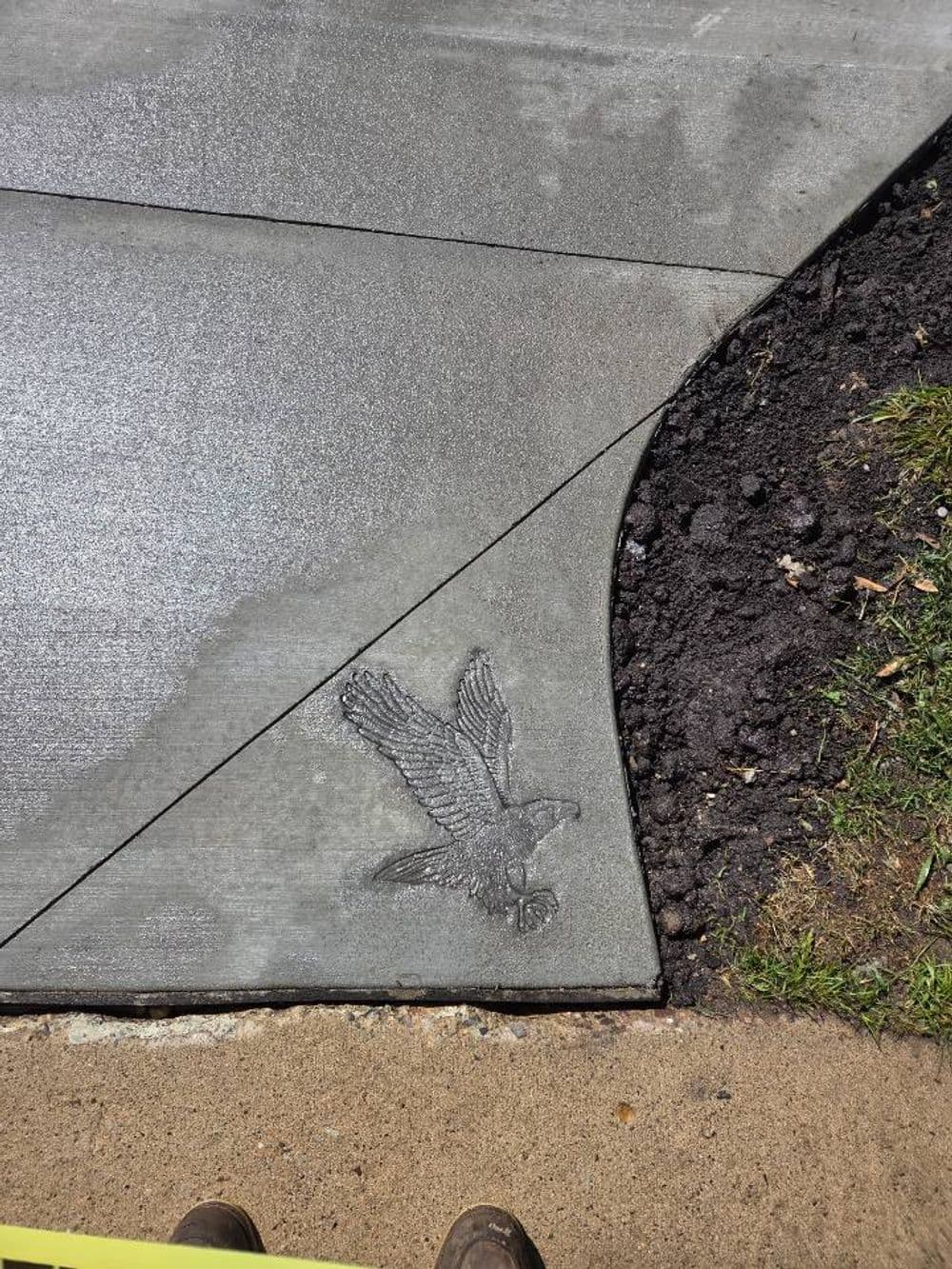 Concrete sidewalk with a detailed eagle imprint in the corner, showcasing artistic design.