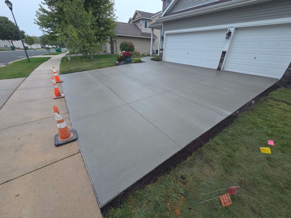 Newly poured concrete driveway next to a residential garage with traffic cones.