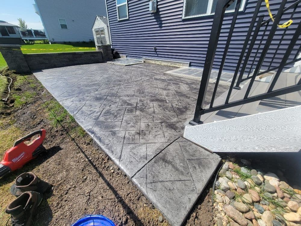 Stamped concrete patio with dark gray finish next to a house and landscaped yard.
