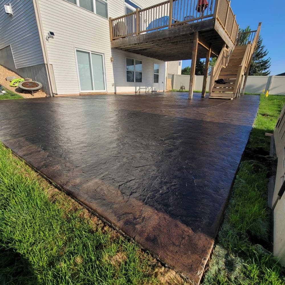 Decorative stamped concrete patio with wooden deck and grassy area, enhancing outdoor space.