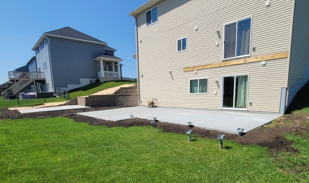 Newly poured concrete patio with grass and house in background on a sunny day.